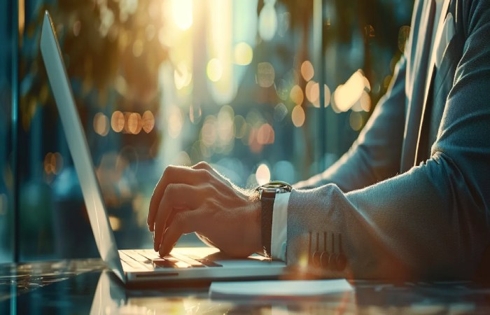 Businessperson typing on a laptop at sunset, drafting a professional request for proposal (RFP).